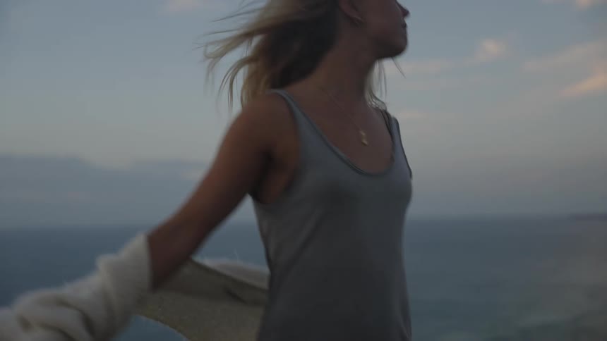 Blondehaired woman gazes at the sea from a cliff at sunset