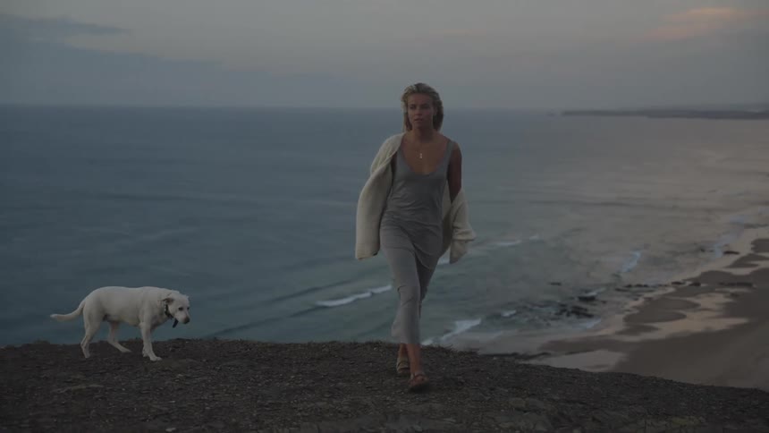 Woman and dog watch the sea from the top of a cliff