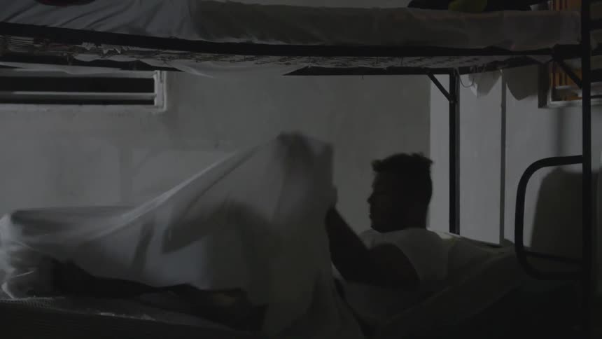 A man lays down on the bottom of a bunk bed and covers himself with a sheet