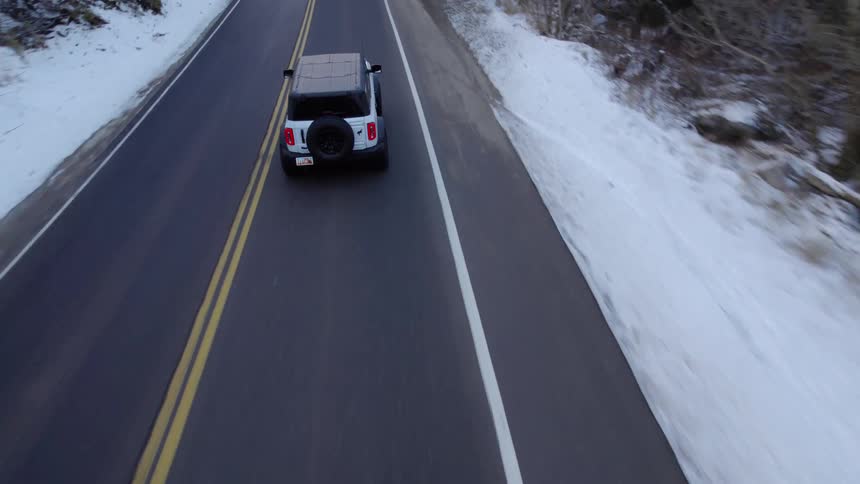 White car driving on a paved road surrounded by snow