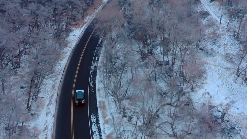 Car drives along a winding road surrounded by trees and snow