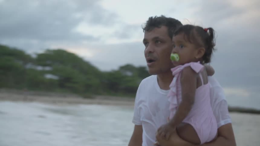 A man walks in the water by the beach with a child