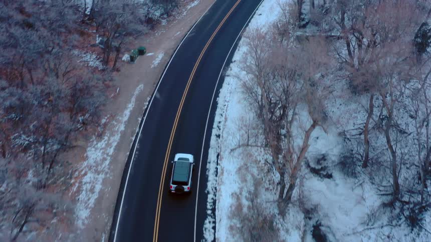 A car drives along a winding road through a snowy forest