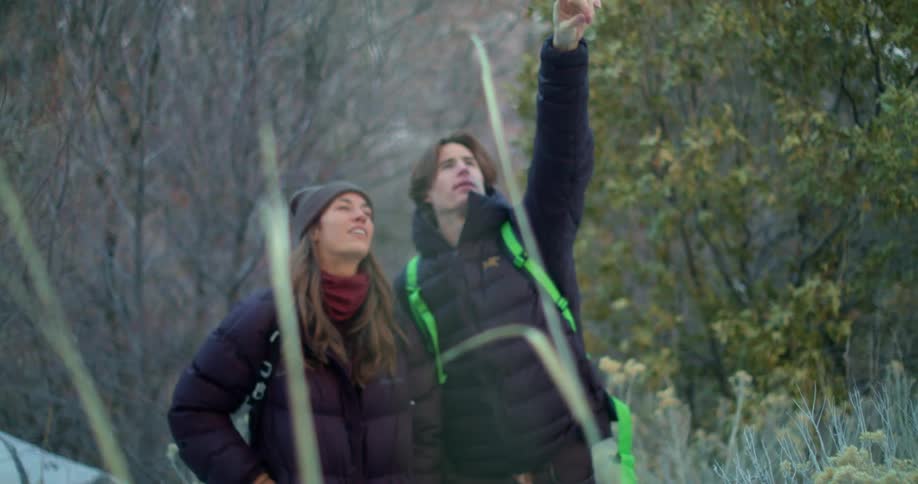 Two young people with backpacks observing and pointing at something in the forest