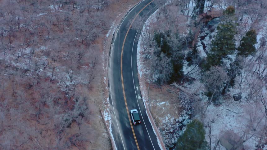 A car drives on the highway during winter with the roads lined by leafless trees at midday
