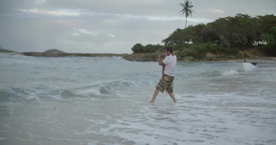 A man holds a young girl on a beach and walks into the ocean waves