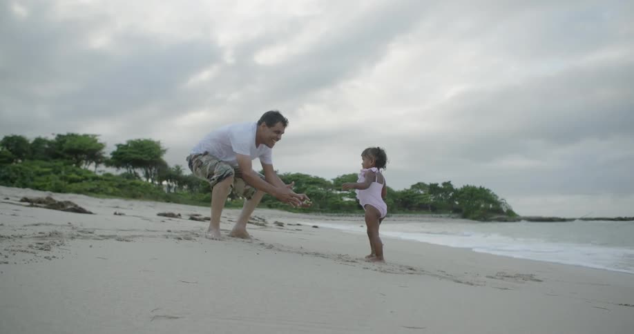 A toddler girl and her father are playing on the beach