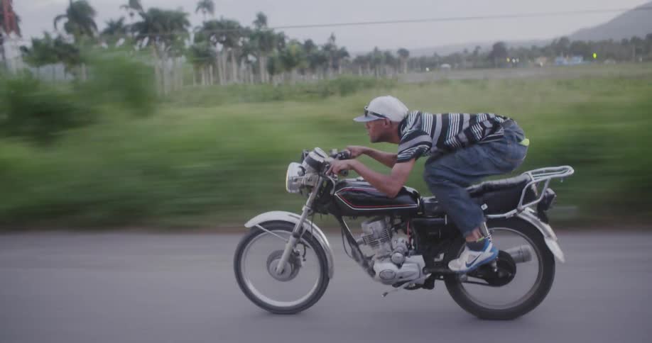 Motorcyclist hunched over and riding very fast down a narrow paved road