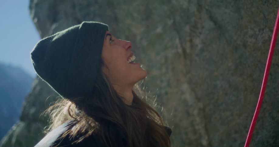 Woman smiles looking upward while holding a climbing rope near a rock wall