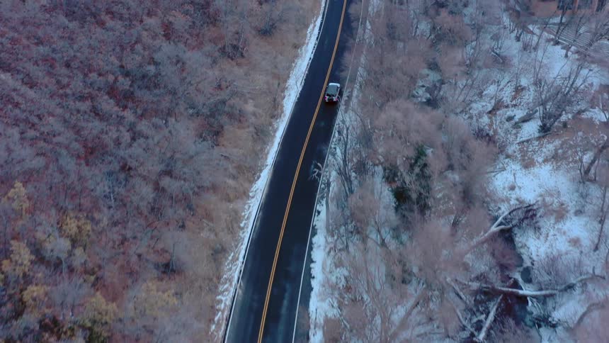 Aerial driving on snow lined road across the wilderness next to a stream and lake