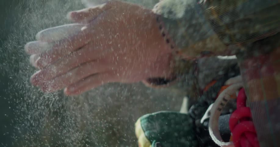 A persons hands shows them covered in white chalk dust as they rub their hands together in preparation for rock climbing