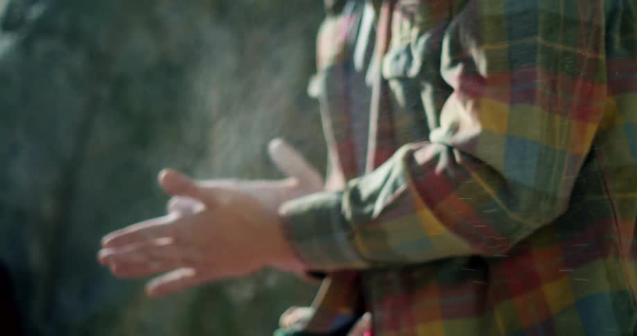 A person in a plaid shirt clapping their hands together to spread climbing chalk creating a cloud of white dust in the air