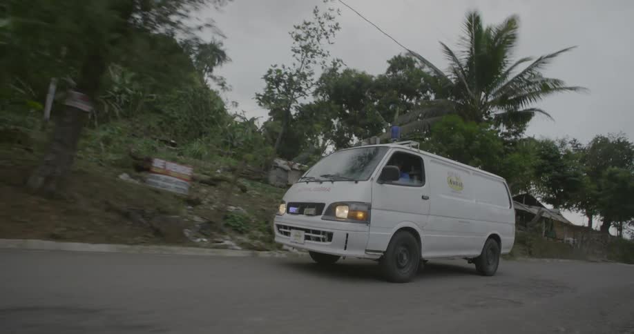 A white van with lights on it speeds down a wooded road