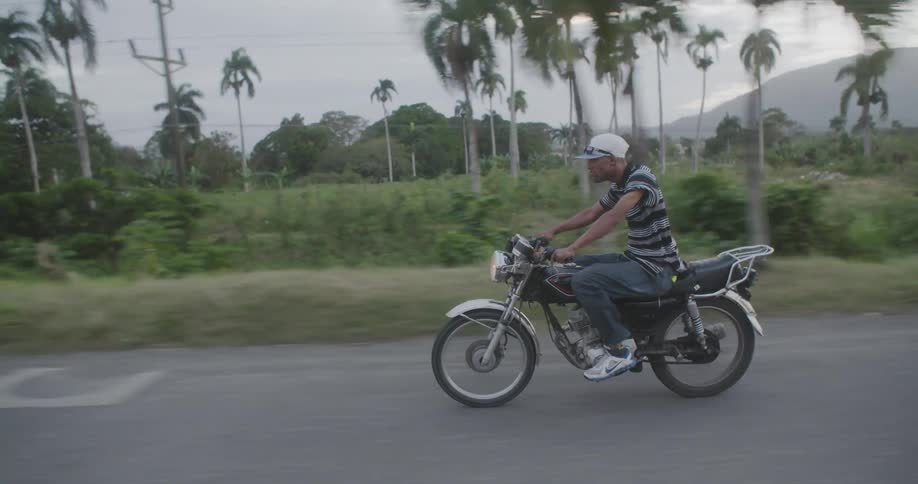 A man rides a motorcycle with palm trees in the distance
