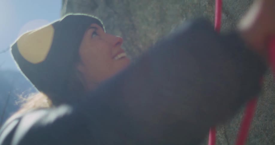 Woman wearing a beanie holds a rope and looks up during climbing