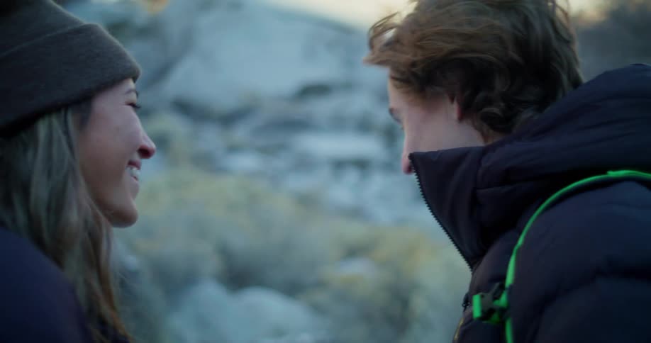 A young couple both wearing winter jackets has a discussion while hiking on a mountain at midday