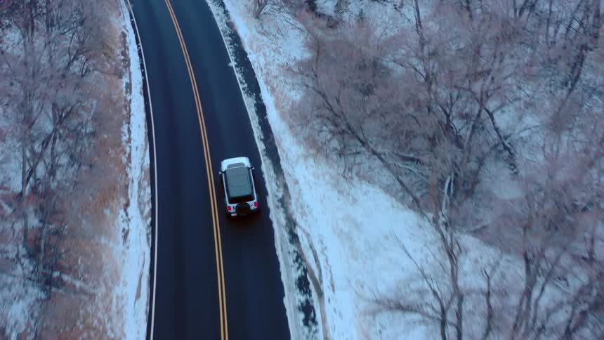Motor vehicle drives along a highway passing snowy woods and a hill on a winter day