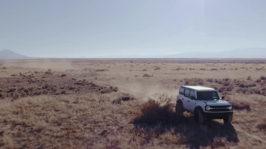 White ford driving on a dirt trail in open field