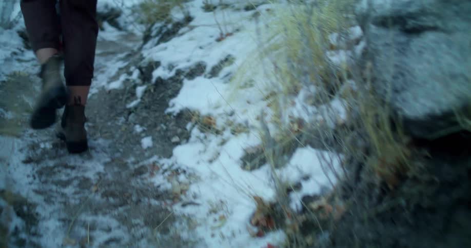 People walk along a narrow trail with patches of snow on the ground