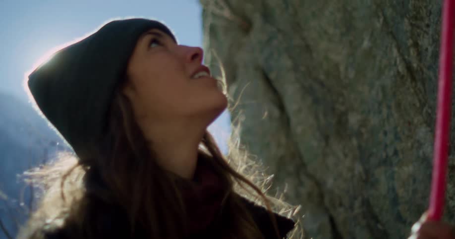 Woman smiles while manipulating a climbing rope and looking up at a cliff on a sunny winter day