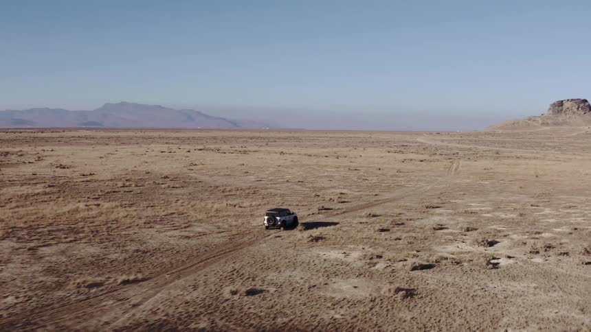 Car drives along a trail in the middle of a vast desert landscape