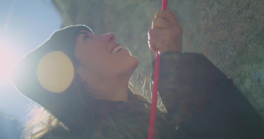 Woman wearing a beanie holds a climbing rope while looking up