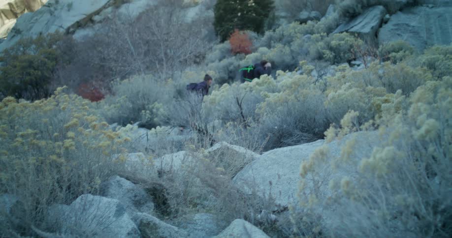 Two backpackers crossing a trail among rocks and dry vegetation