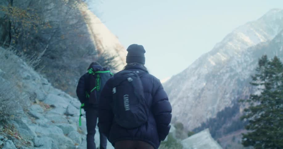 A man and woman are hiking up a rocky trail in a mountain range