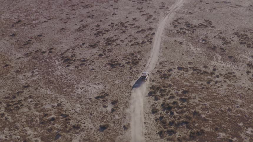 Vehicle travels along a dirt road in an arid area seen from above