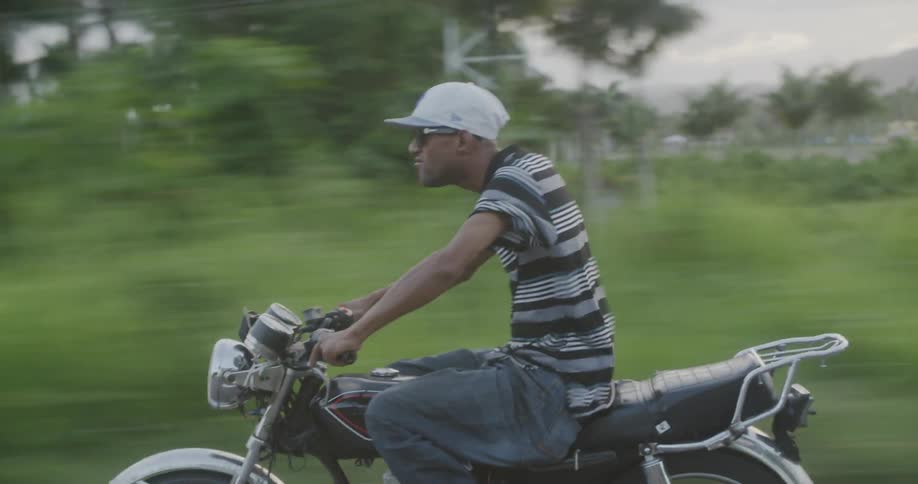 A man rides a motorcycle in a tropical area
