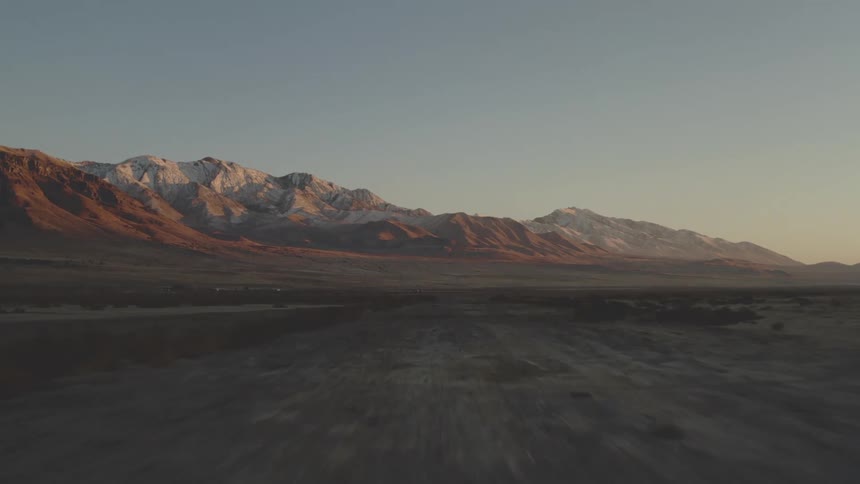 A desert region of land with huge mountains in the background on a day with blue skies