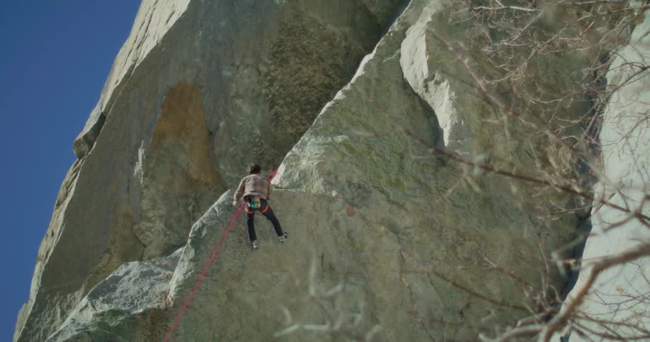 Man climbs a large rock wall with a safety rope