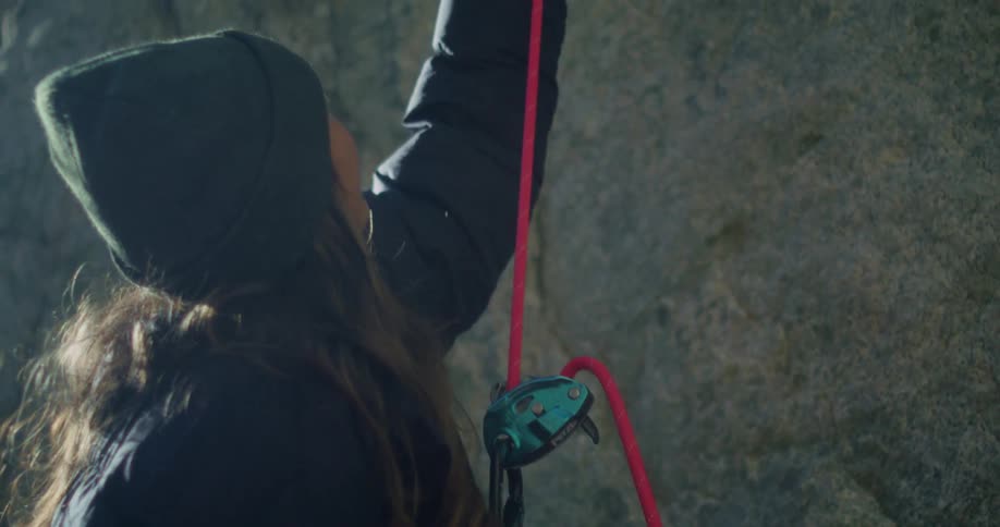 A woman climbs a mountain rock face with a rope