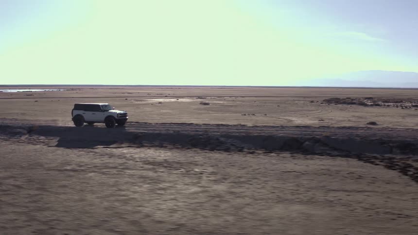 White car driving on a dirt road in a desert area