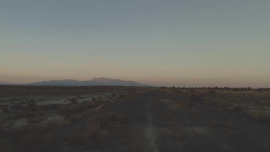 A black dirt road in a desert region with mountains in the background on a morning with blue and orange skies