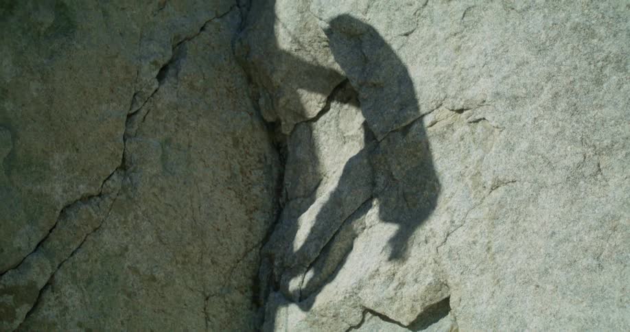 The shadow of a person can be seen as they attempt rock climbing