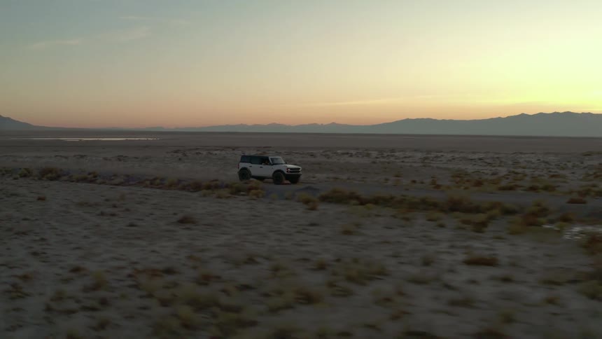White suv driving on a dirt road in the desert at sunset