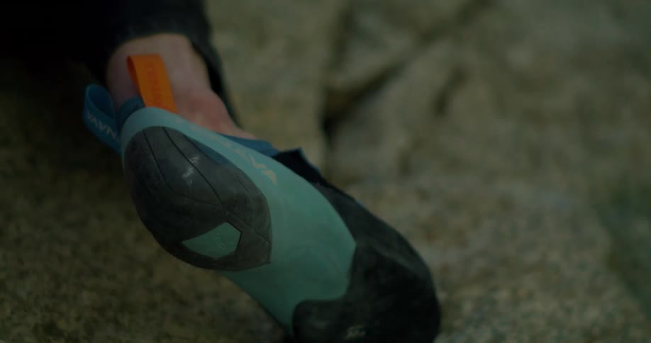 Foot wearing a blue climbing shoe presses against a crack in the rock while ascending