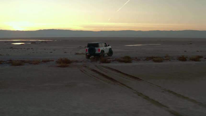 A white suv drives across the desert at sunset leaving fresh tire tracks behind