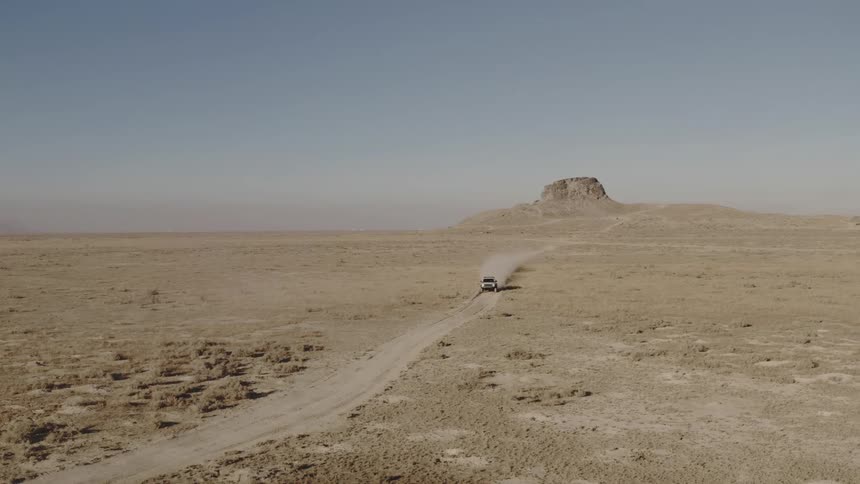 Jeep traveling on a dirt road through the desert with a rock formation in the distance