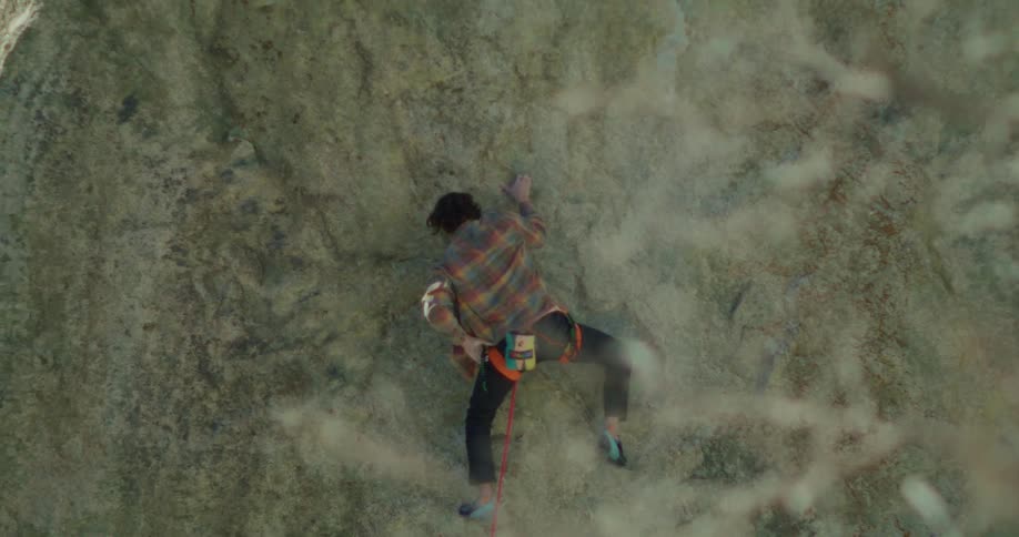 A person rock climbing a large textured cliff face moving deliberately upward while a safety rope hangs below them