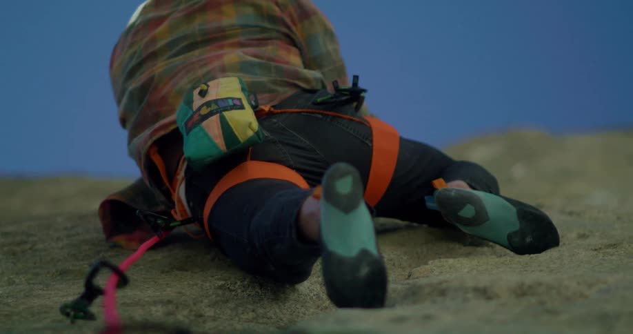 A closeup of a persons feet and legs as they rock climb a vertical rock face outdoors