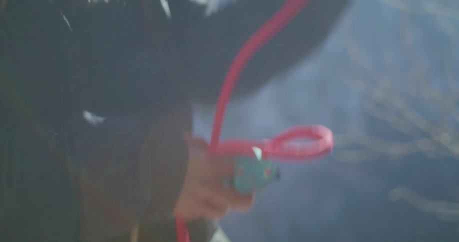A person is handling a bright red rope and a carabiner the person is wearing a black jacket and a harness suggesting they are rock climbing