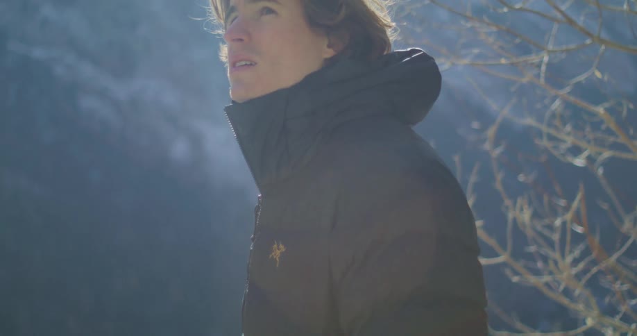 Man in a jacket looks upward in a sunlit mountainous setting