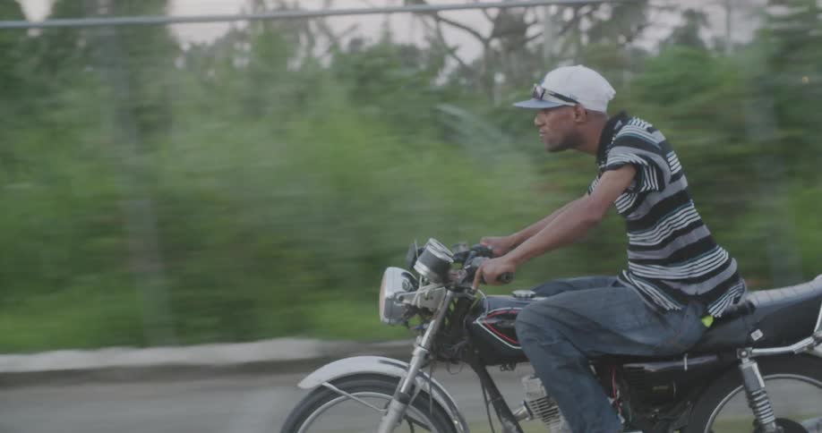 A man in a striped shirt rides a motorcycle