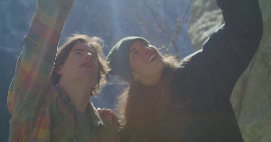 Two young people are looking up with expressions of awe and joy with sun rays shining through the misty air