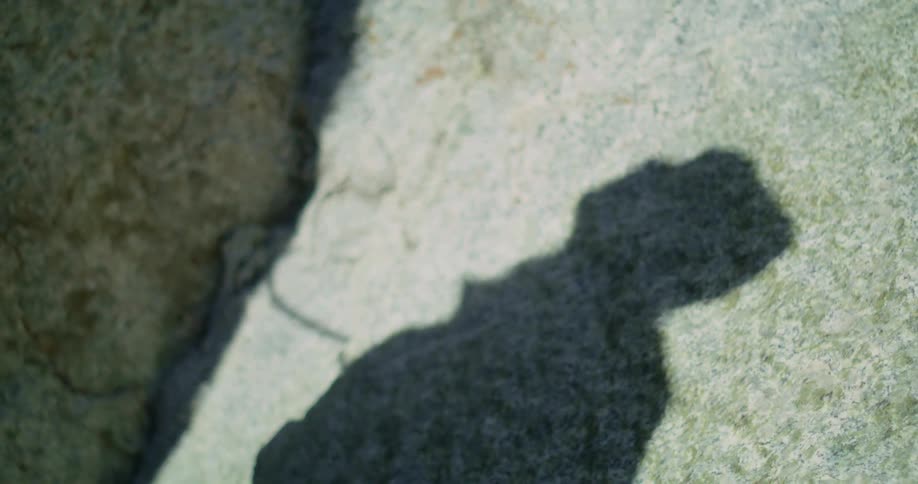 Shadow of a man on rock looking upwards he is holding something