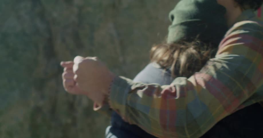 A couple is embracing outdoors the man is wearing a plaid shirt and the woman is wearing a green beanie