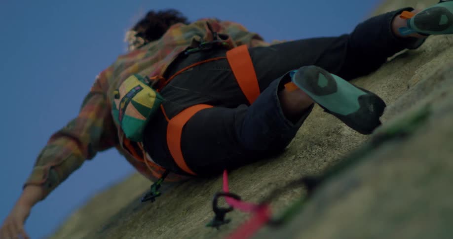 Rock climber uses a harness and rope while climbing a cliff under a blue sky
