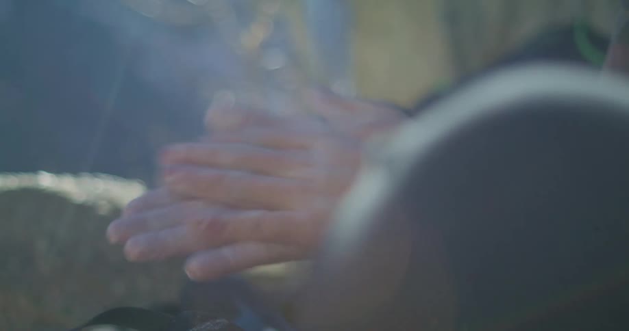 The man sits by the mountain rubbing his hands together